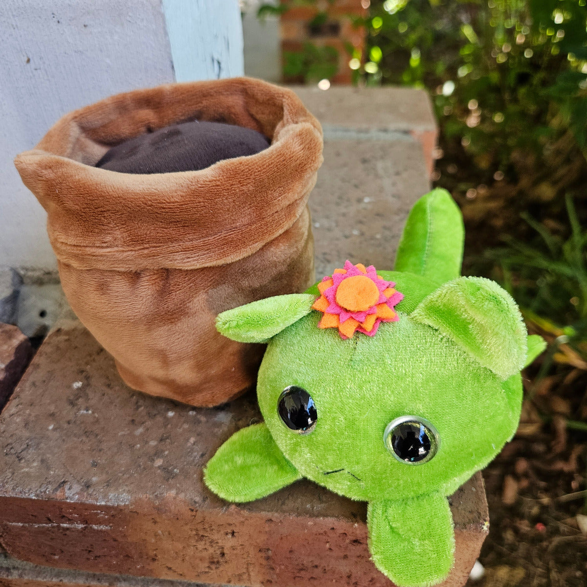 Green plush toy with a flower on a brown pipe against a natural background