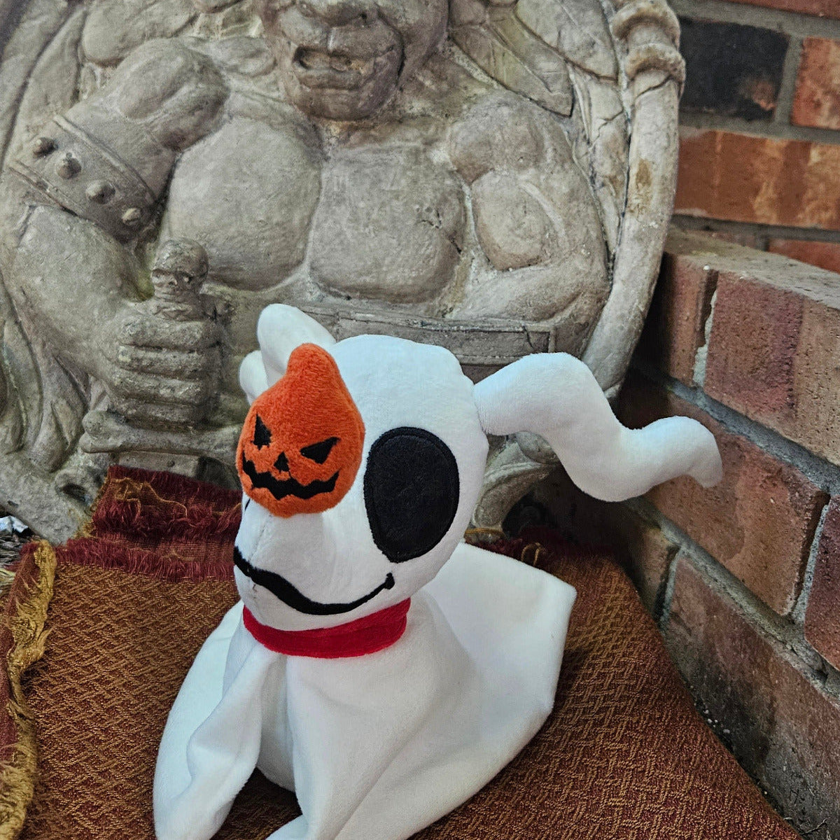 Stuffed animal with pumpkin head in front of stone wall and brick background