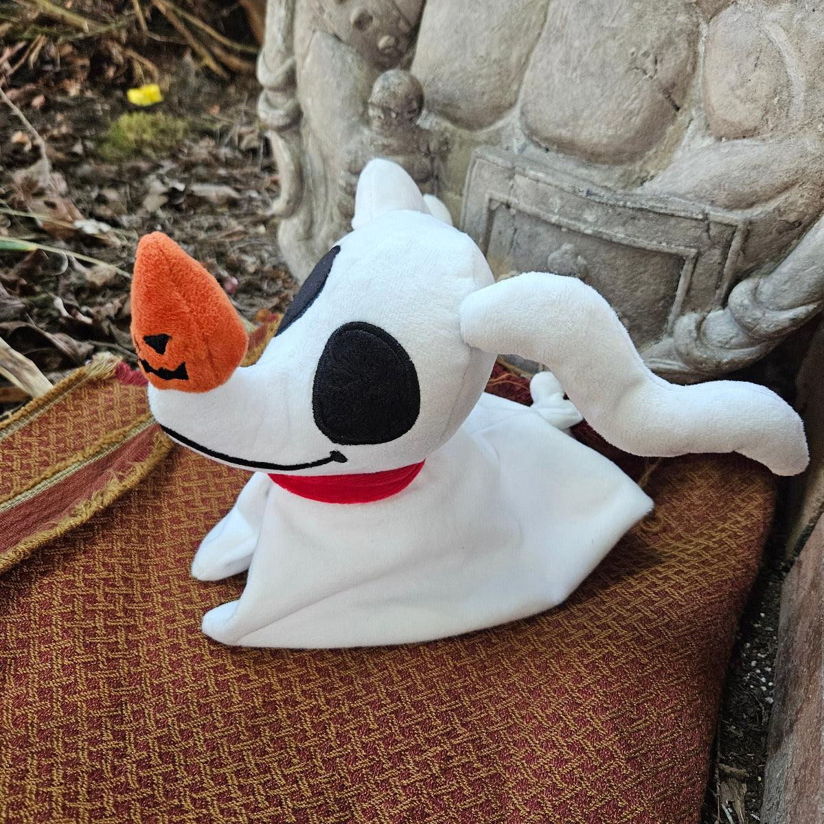 White plush toy resembling a ghost with black eyes and orange nose on a textured surface.