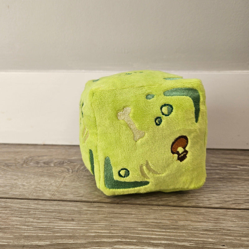 Green plush toy with animal designs on a wooden surface