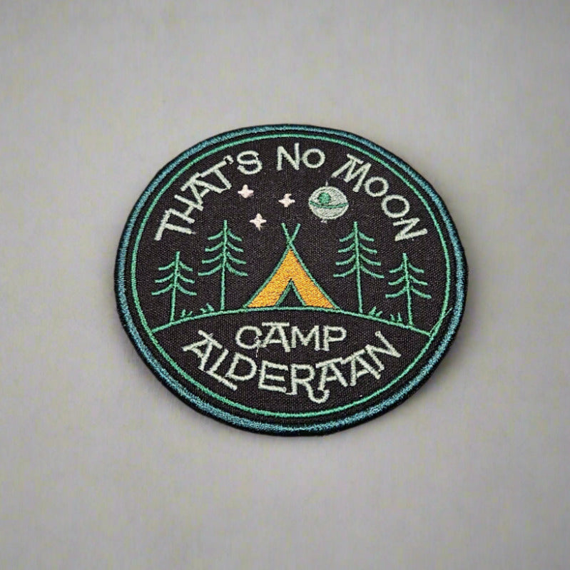 Circular patch with 'That's No Moon Camp Alderaan' text and camping design on a light gray background
