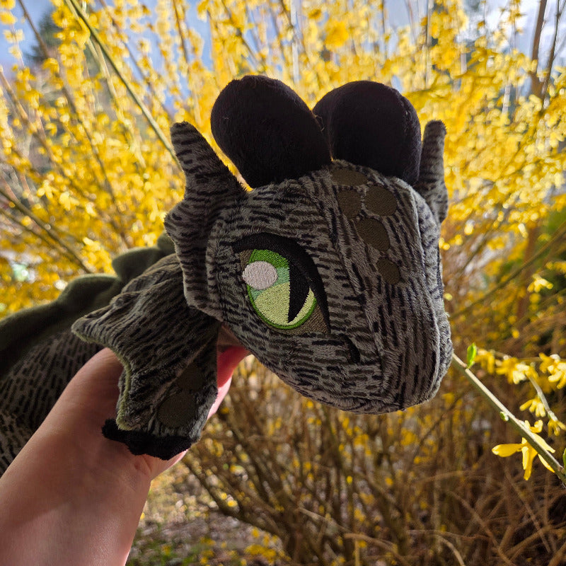 Plush toy resembling a dragon held by a hand with yellow flowers in the background