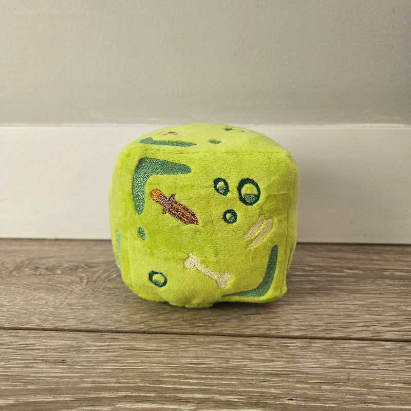 Green plush dice with embroidered details on a wooden surface