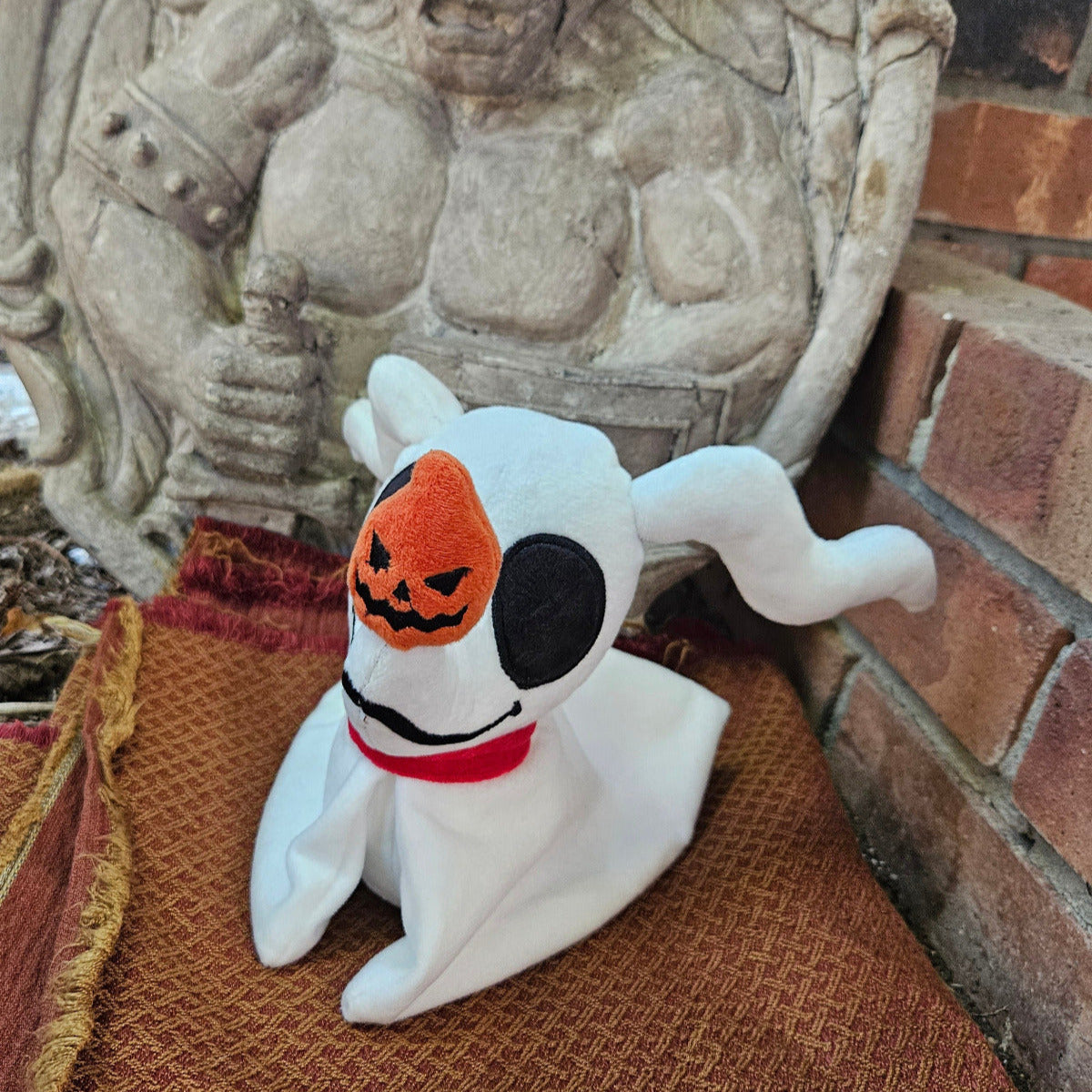 White dog plush toy with pumpkin face on a brown mat against a stone wall.