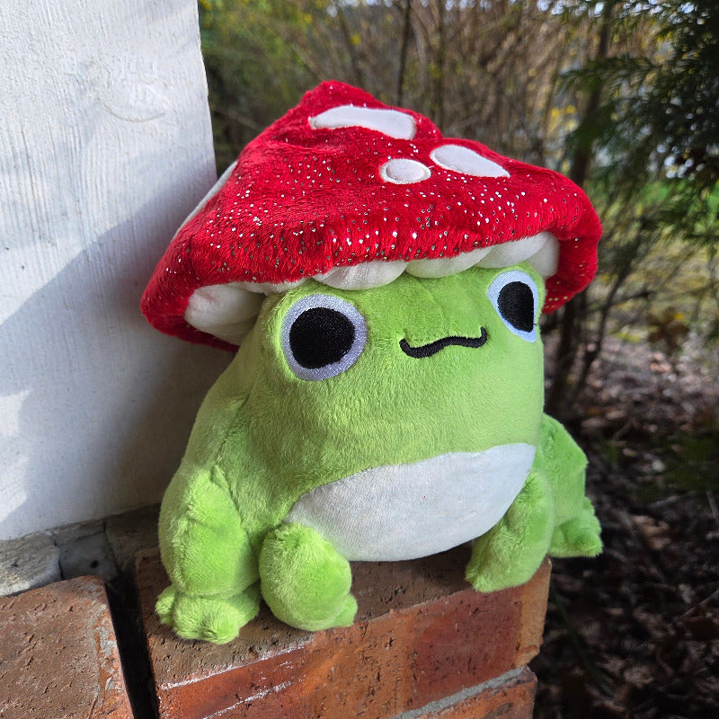 Green plush toy with a red mushroom cap on a wooden surface outdoors