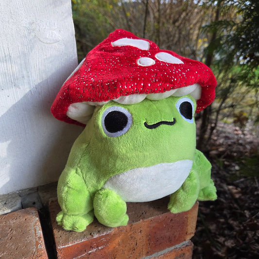 Green plush toy with a red mushroom cap on a wooden surface outdoors