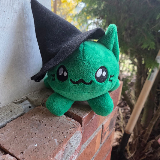 Green plush toy with black hat on a brick surface