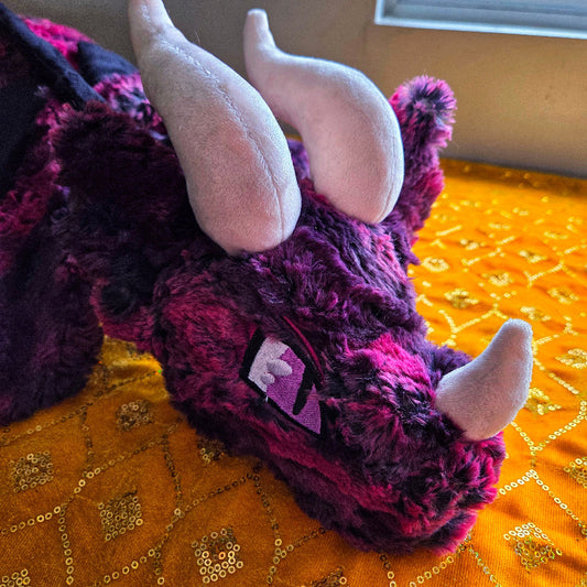 Purple plush dragon toy with white horns on a yellow patterned surface