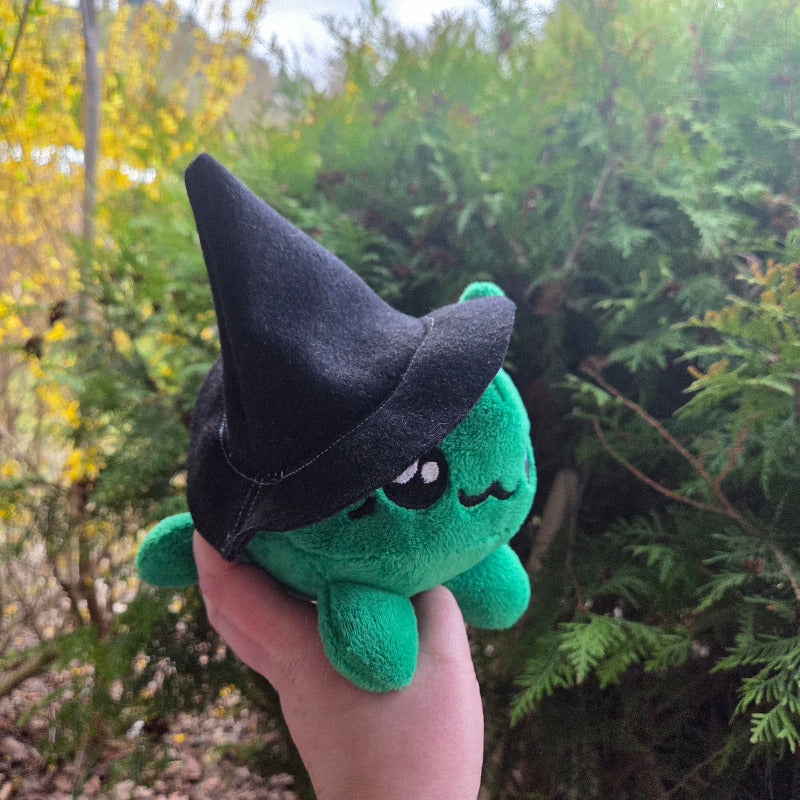 Green plush toy with black hat on a brick surface