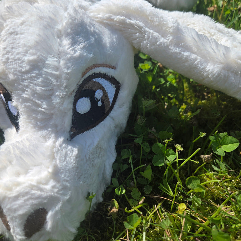 Close-up of a white plush dog toy with brown spots lying on grass.