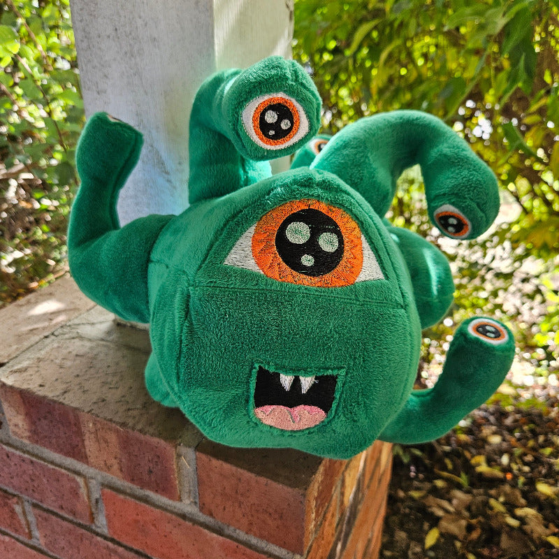 Green plush toy with large eyes on a wooden surface outdoors