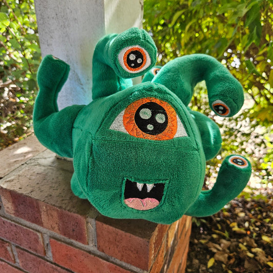 Green plush toy with large eyes on a wooden surface outdoors
