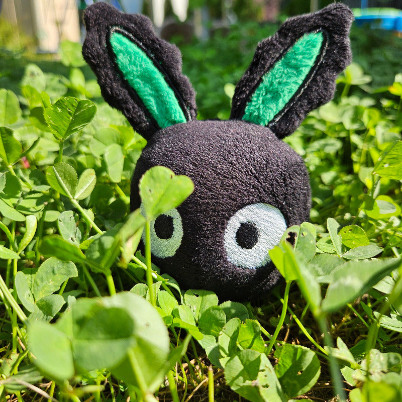 Plush toy bee with green wings and black body in a grassy area