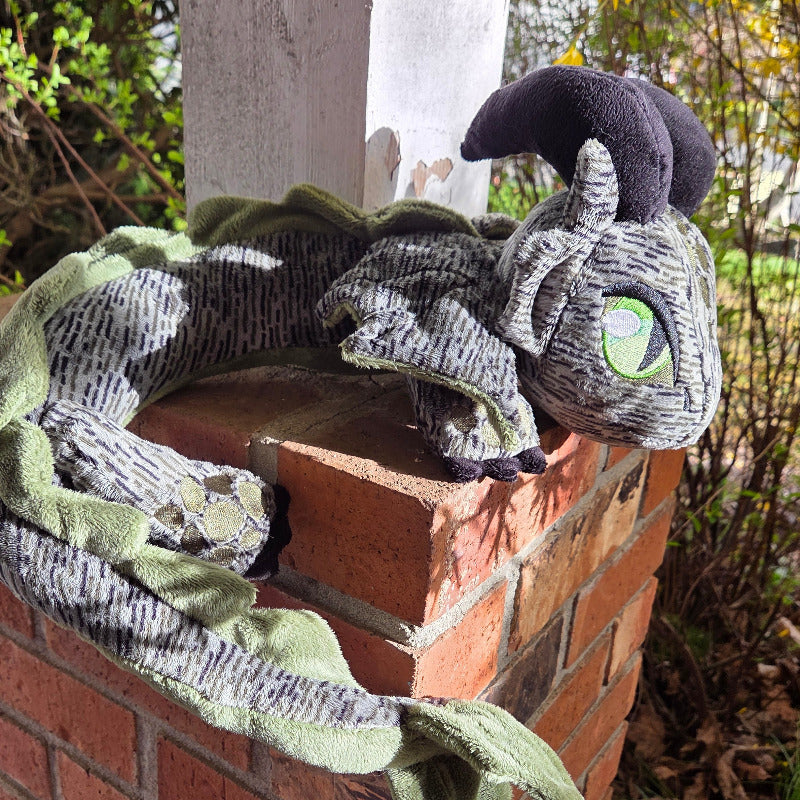 Plush dragon toy on a brick surface with a natural background
