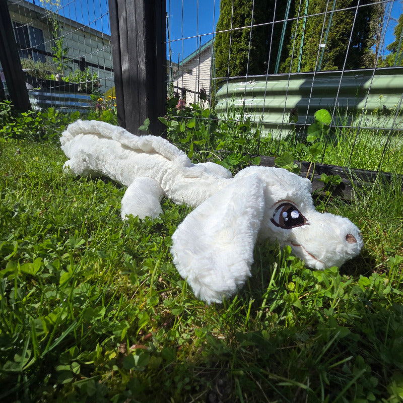 White plush toy resembling a dragon on grass with buildings in the background