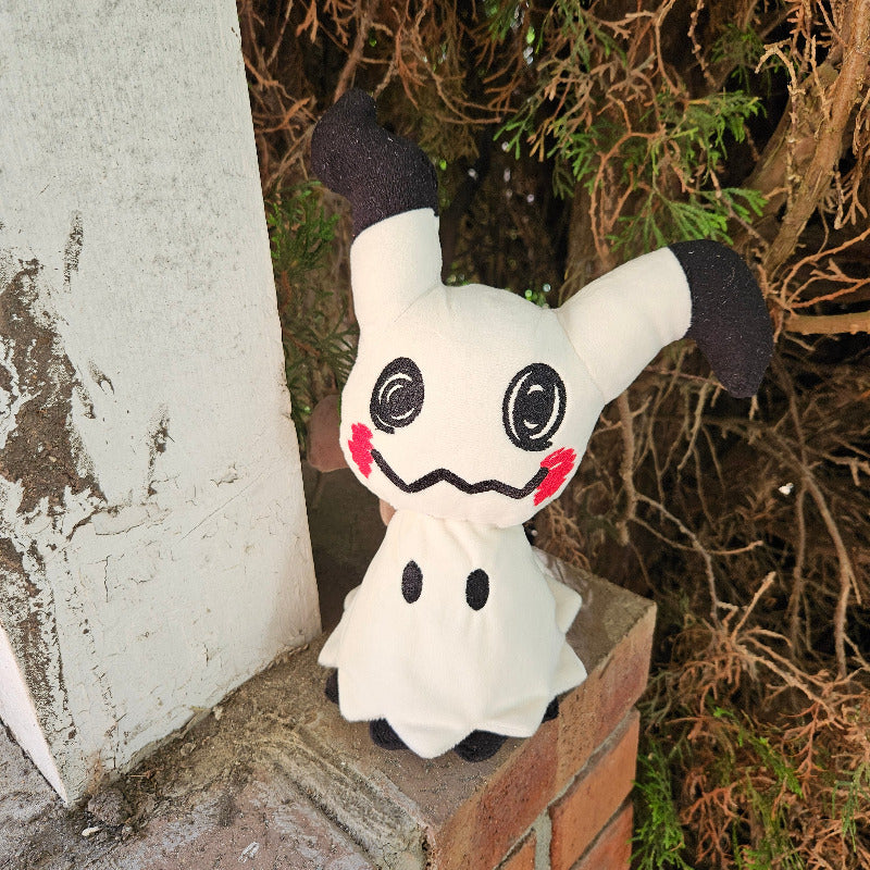 Plush toy resembling a ghost character on a brick ledge with foliage in the background