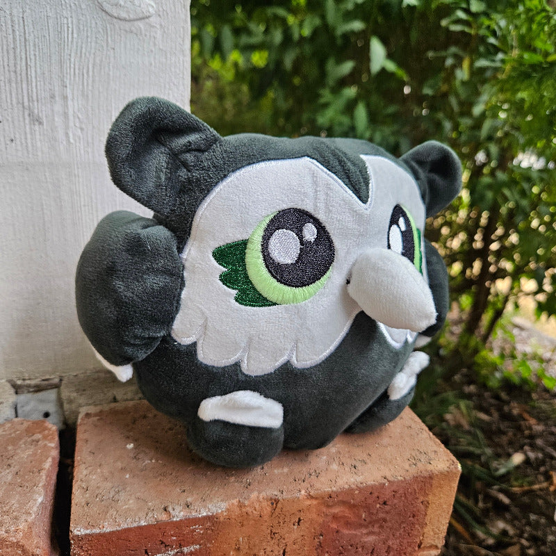 Plush toy resembling a cartoon character on a brick surface with greenery in the background