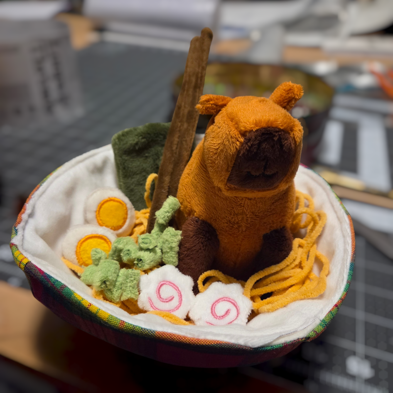 Plush toy bear in a bowl with noodles and vegetables on a blurred kitchen background