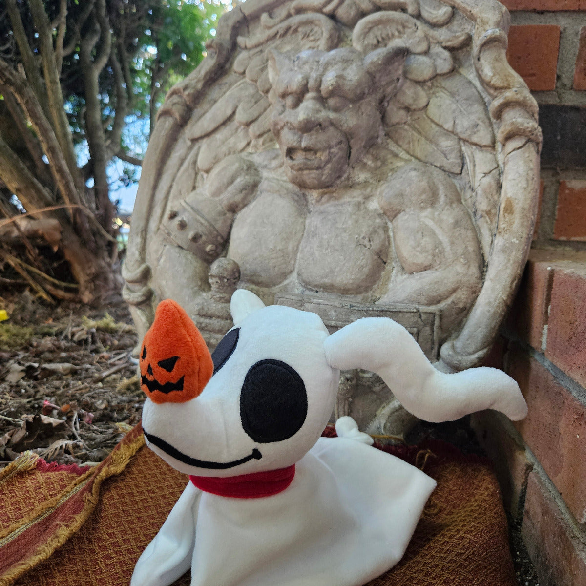 Plush ghost toy with pumpkin nose next to stone sculpture of a face with long hair.