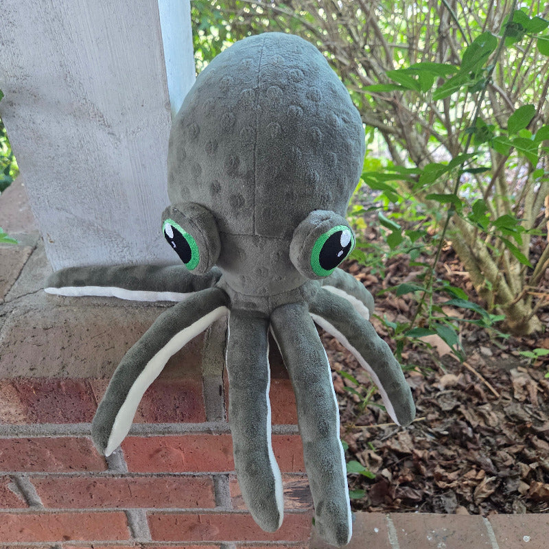 Plush octopus toy against a brick wall with greenery
