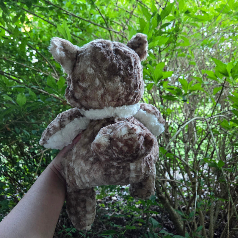 Plush owl bear toy held in front of a green leafy background
