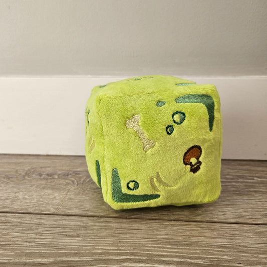 Green plush toy with animal designs on a wooden surface