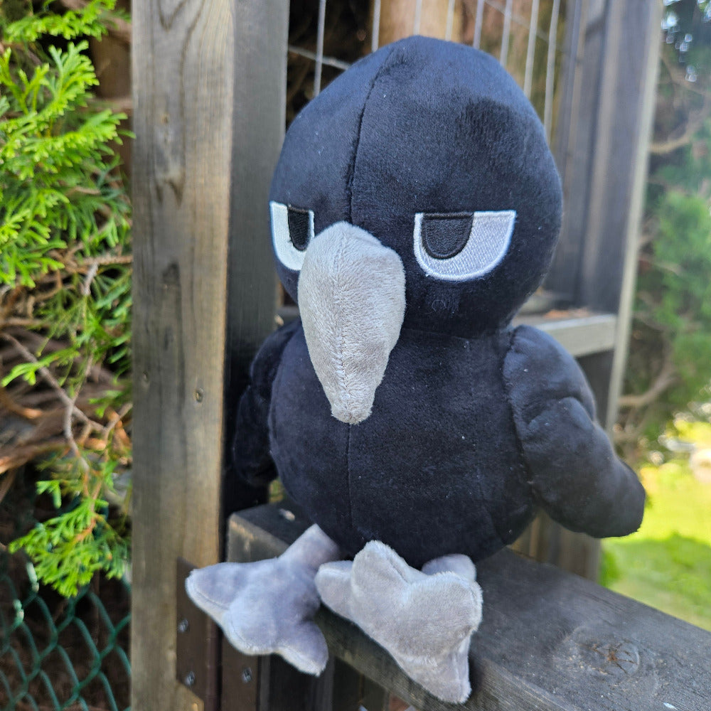 Plush toy penguin on a wooden surface with greenery in the background