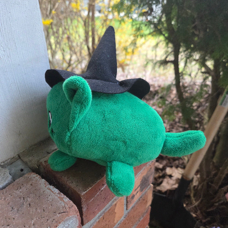 Green plush toy with black hat on a brick surface