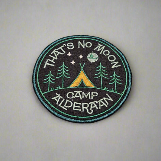 Circular patch with 'That's No Moon Camp Alderaan' text and camping design on a light gray background