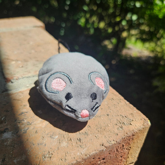 Gray mouse-shaped object with pink cheeks on a stone surface