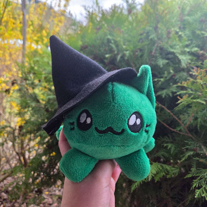 Green plush toy with black hat on a brick surface