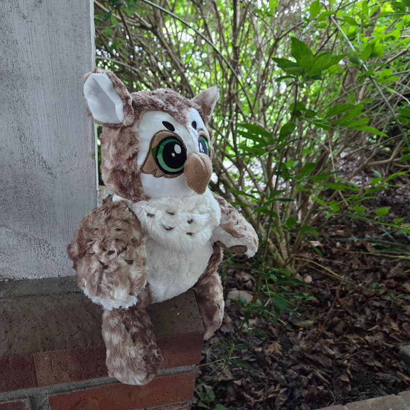Plush owl toy on a brick ledge with greenery in the background