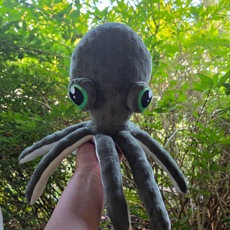 Plush octopus toy held in front of a green leafy background