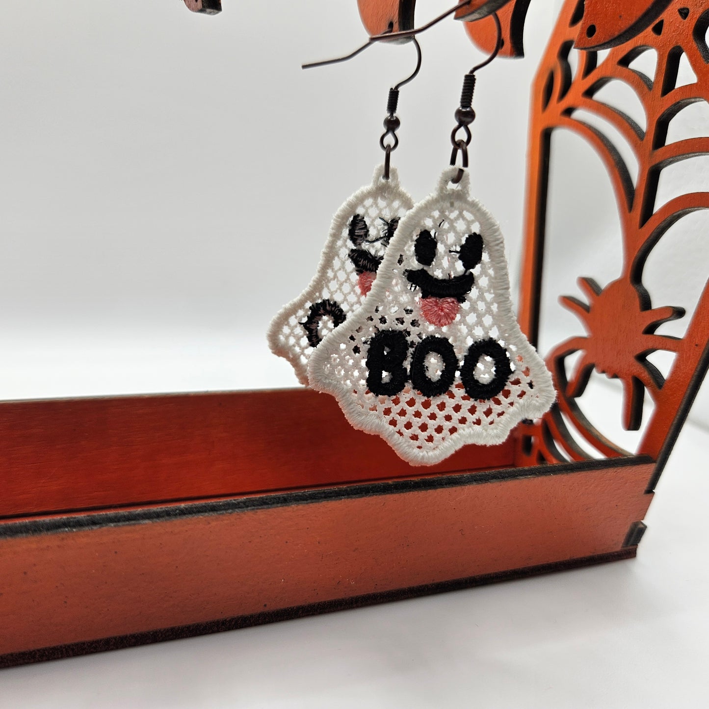 Halloween-themed ghost earrings with 'BOO' text on a decorative stand.