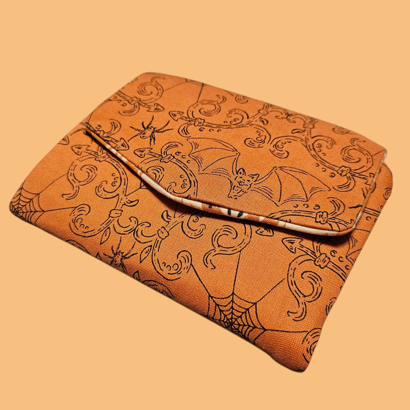 Brown leather pouch with bat and spider web pattern on a beige background