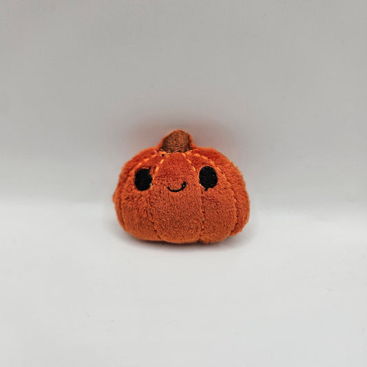 Small brown plush toy shaped like a pumpkin on a light gray background