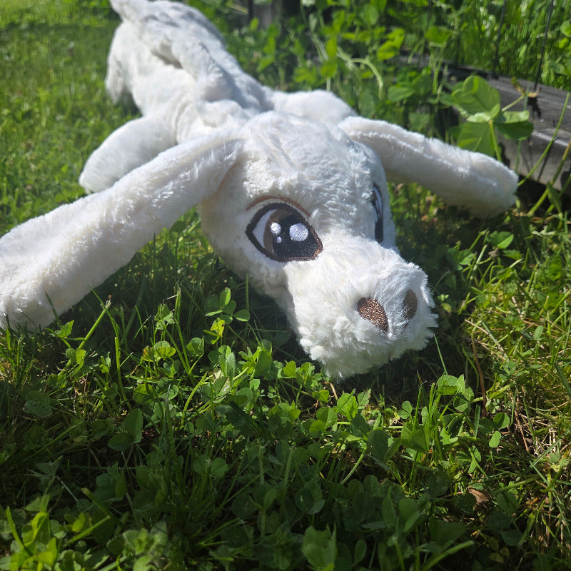 White plush toy with black eyes lying on green grass