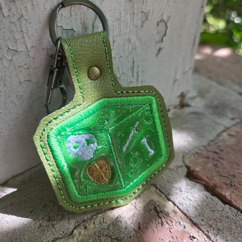 Green embroidered keychain with a leaf design on a stone surface