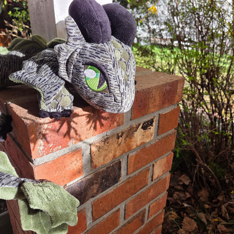 Toy dragon on a brick surface with greenery in the background