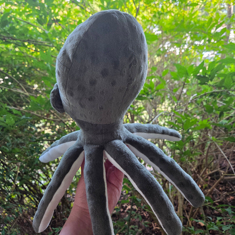 Plush octopus toy held in front of a green leafy background