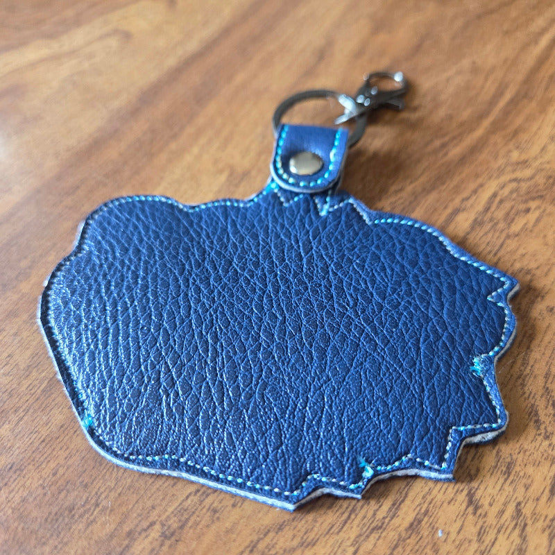 A blue textured leather keychain or bag charm with a silver metal clasp, resting on a wooden surface.