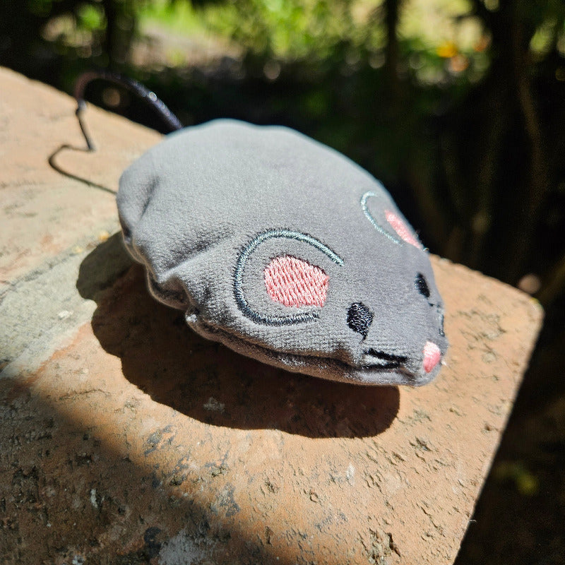 Gray plush toy resembling a cat on a textured surface with a blurred natural background