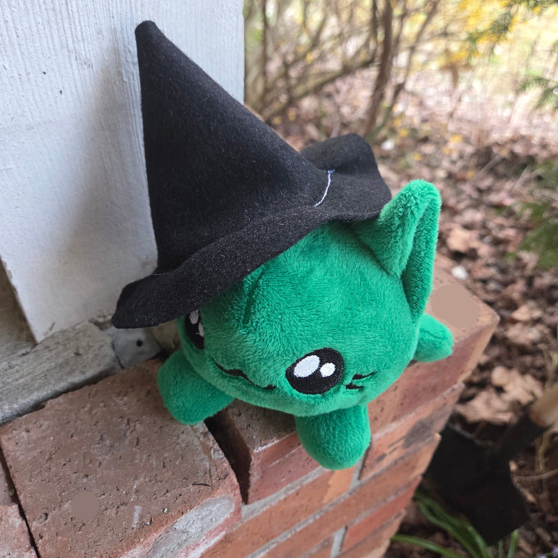 Green plush toy with black hat on a brick surface